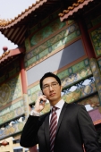 Businessman standing in front of temple gate, using mobile phone - Alex Mares-Manton