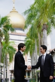 Two businessmen shaking hands, Mosque in the background - Alex Mares-Manton