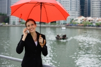 Businesswoman under red umbrella, using mobile phone, river in the background - Alex Microstock02