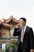 Businessman standing in front of Chinese temple, using mobile phone - Wang Leng