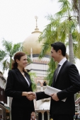 Businessman and businesswoman shaking hands, Mosque in the background - Wang Leng