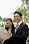 Businessman and businesswoman with newspaper, smiling at camera - Wang Leng