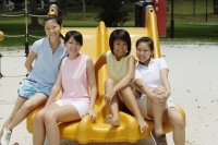 Young women sitting on slide in playground, smiling at camera - Alex Microstock02