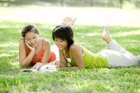 Two young women lying on grass, looking at magazine - Alex Microstock02