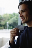 Man holding credit card, smiling, looking out the window - Yukmin