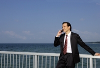 Businessman leaning on railing, using mobile phone - Yukmin