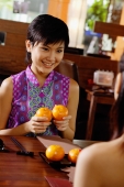 Young woman holding two oranges, smiling at person in front of her - Wang Leng