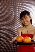 Young woman holding a tray with two oranges, smiling at camera - Alex Microstock02