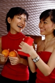 Young women holding two oranges and red packet, smiling at each other - Alex Microstock02