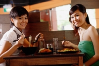 Two young women sitting at table in restaurant, smiling at camera - Alex Microstock02