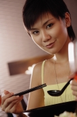 Young woman holding chopsticks and spoon, looking at camera - Alex Microstock02