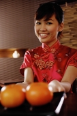 Young woman in Chinese dress holding a tray with two oranges, smiling at camera - Alex Microstock02