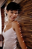 Young woman leaning on bamboo screen, smiling - Alex Microstock02