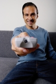 Man holding TV remote control, pointing towards camera - Yukmin