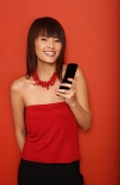 Young woman in red tube top, standing against red wall, holding mobile phone - Yukmin