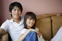 Couple sitting on sofa, smiling at camera - Yukmin