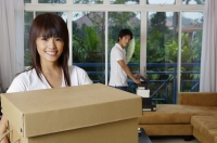 Woman carrying a box, smiling at camera, man in the background - Yukmin