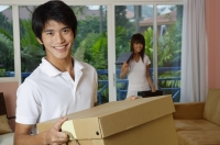 Man carrying a box, smiling at camera, woman in the background - Yukmin