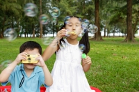 Girl blowing bubbles, boy taking pictures with camera - Yukmin