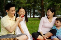 Family of four in park, father feeding daughter an apple - Yukmin