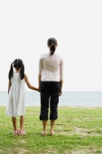 Mother and daughter, standing, looking out to sea, rear view - Yukmin