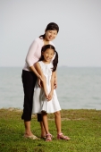 Mother with daughter, standing by beach, smiling at camera - Yukmin