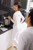 Woman cooking on stove, looking over shoulder at man standing behind her - Alex Mares-Manton
