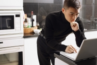 Man in kitchen, looking at laptop - Alex Mares-Manton