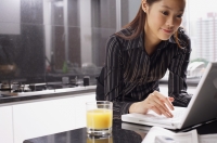 Female executive leaning on kitchen counter using laptop - Alex Mares-Manton