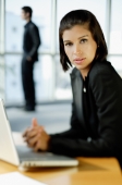 Businesswoman in front of laptop, man in the background - Alex Mares-Manton