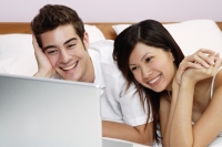 Couple lying on bed, looking at laptop - Yukmin