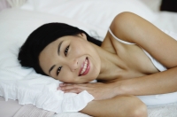 Woman lying on bed, smiling at camera - Yukmin