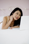 Woman lying on bed, using laptop, hand on neck - Yukmin