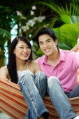 Couple sitting on hammock, smiling at camera - Yukmin