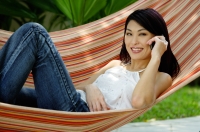 Woman lying on hammock, using mobile phone - Yukmin