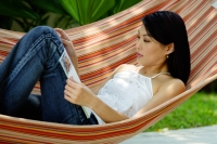 Woman lying on hammock, reading magazine - Yukmin