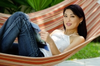 Woman lying on hammock with magazine - Yukmin