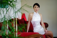 Woman dressed in white Chinese cheongsam, sitting on red sofa - Yukmin