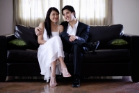Well dressed couple sitting on sofa, smiling at camera - Yukmin