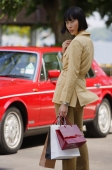 Woman with shopping bags, turning to look at camera, car in the background - Alex Mares-Manton