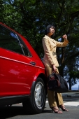 Woman leaning on red car, carrying bag, looking at watch - Alex Mares-Manton