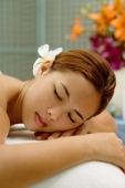 Young woman with flower in hair, lying on massage table, eyes closed - Alex Microstock02