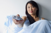 Woman sitting up in bed, holding TV remote control - Alex Mares-Manton