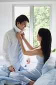 Couple in bedroom, woman adjusting man's tie - Alex Mares-Manton