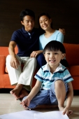 Young boy sitting on floor, parents in background sitting on sofa - Alex Microstock02
