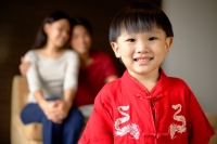 Young boy in red shirt smiling at camera, parents in background - Alex Microstock02