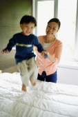 Young boy jumping on bed, mother holding his hand - Alex Mares-Manton