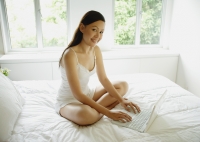 Woman sitting on bed, using laptop, smiling at camera - Alex Mares-Manton