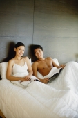 Couple sitting up in bed, with book and magazine, smiling at camera - Alex Mares-Manton