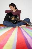 Man holding guitar, sitting cross-legged on floor, looking down - Yukmin